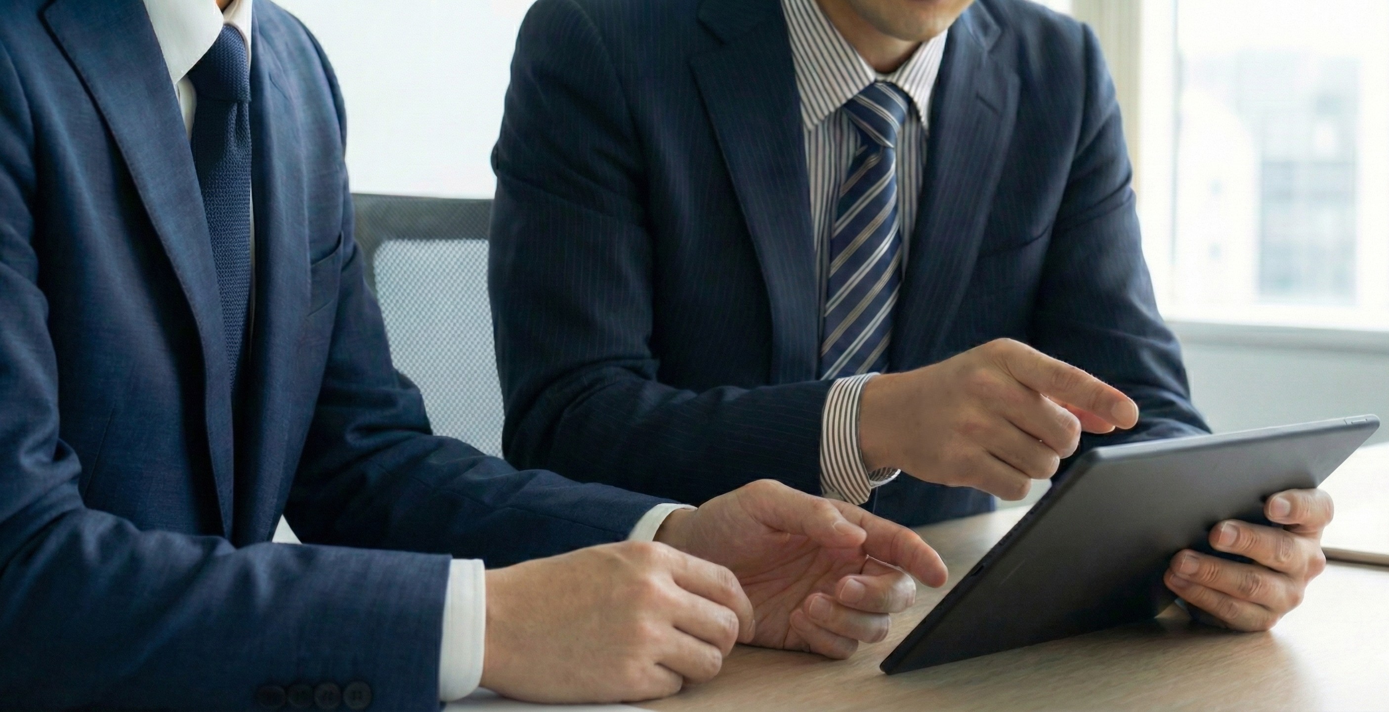 タブレット端末の画面を見ながら打ち合わせをしている2人の男性